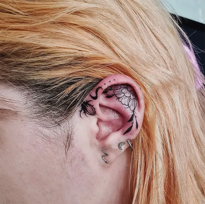 Floral ear tattoo design with intricate black ink detailing on a person's ear.