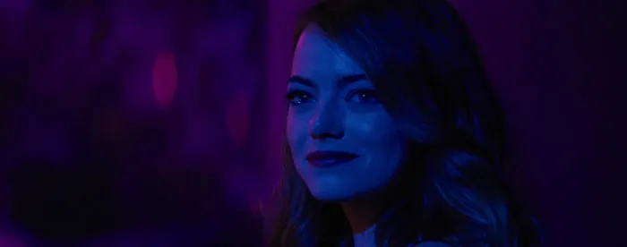 Actress in blue and purple lighting, smiling slightly while looking ahead, representing highest-paid actors.