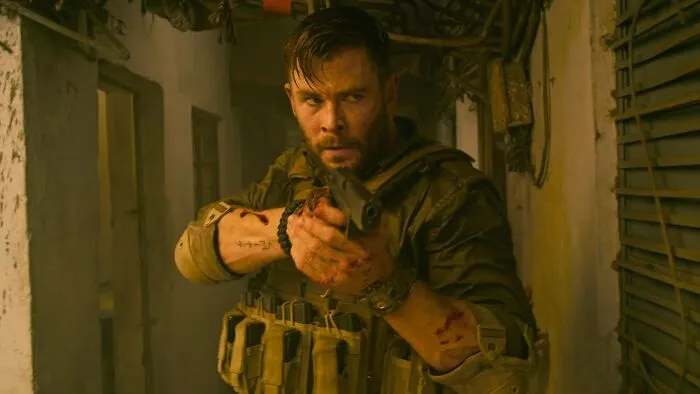 Actor in military gear aiming a gun in a tense scene, representing one of the highest-paid actors of all time.