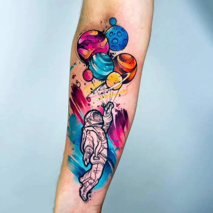 Colorful space tattoo of an astronaut holding planet balloons on a forearm.