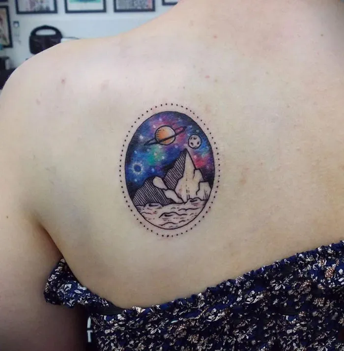 Space tattoo featuring planets and mountains on a person's shoulder.