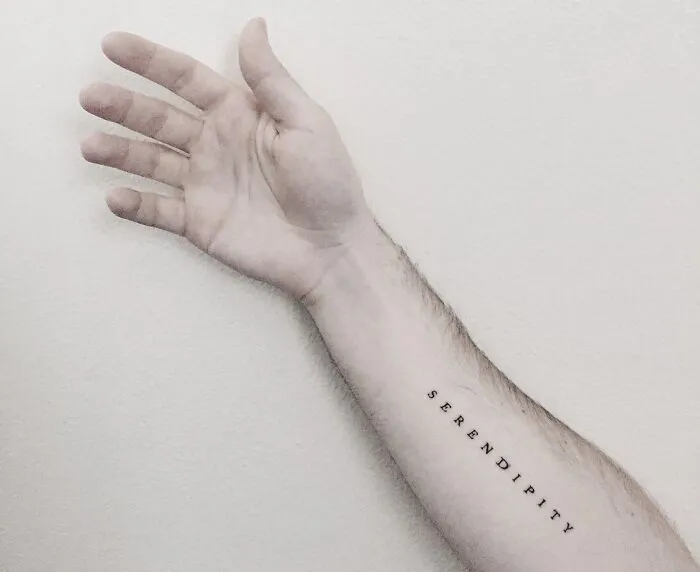 Arm with "serendipity" tattoo in black ink, showcasing a minimalist word tattoo design.