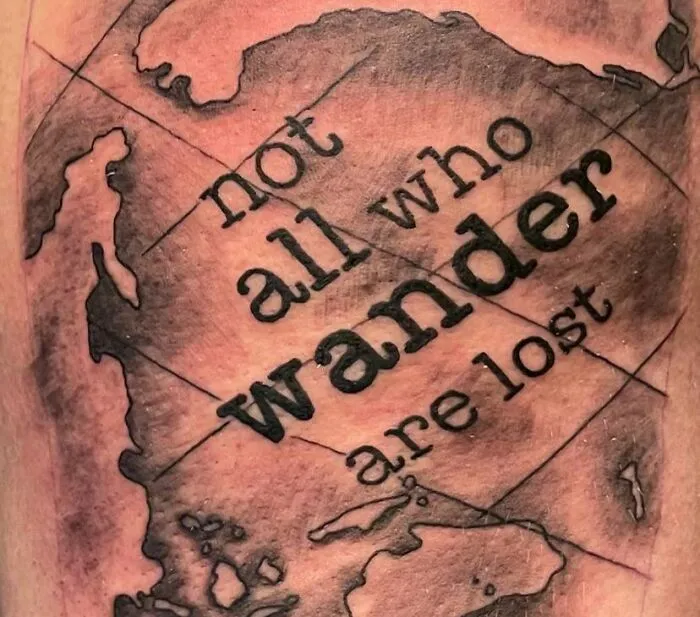Tattoo of text "not all who wander are lost" on a map-themed background, highlighting unique word art on the skin.