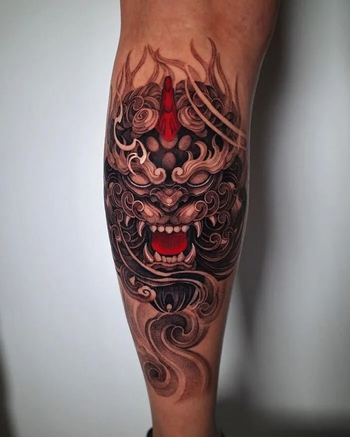 Ornate lower leg tattoo featuring a fierce mythical creature with intricate patterns and vibrant red accents.