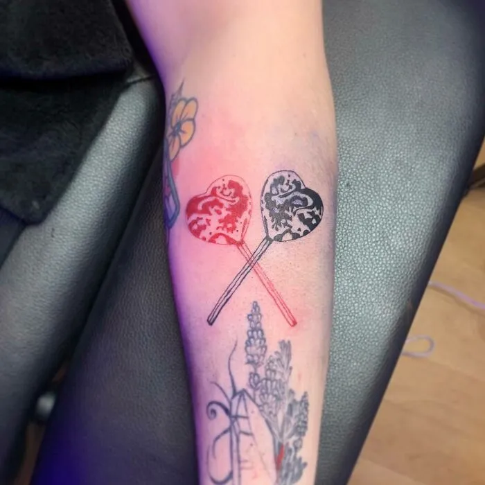 Red ink heart lollipop tattoos on arm, showcasing bold color and intricate design.