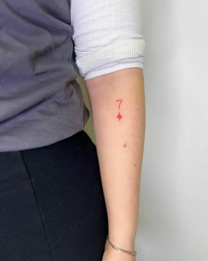 Red ink tattoo of the number 7 with a star on a person's forearm.