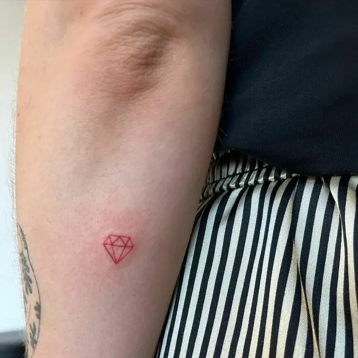 Red ink tattoo of a geometric diamond on an arm.