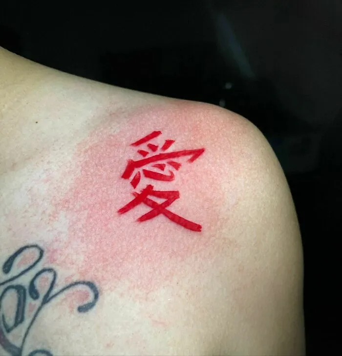 Red ink tattoo featuring Chinese characters on shoulder.