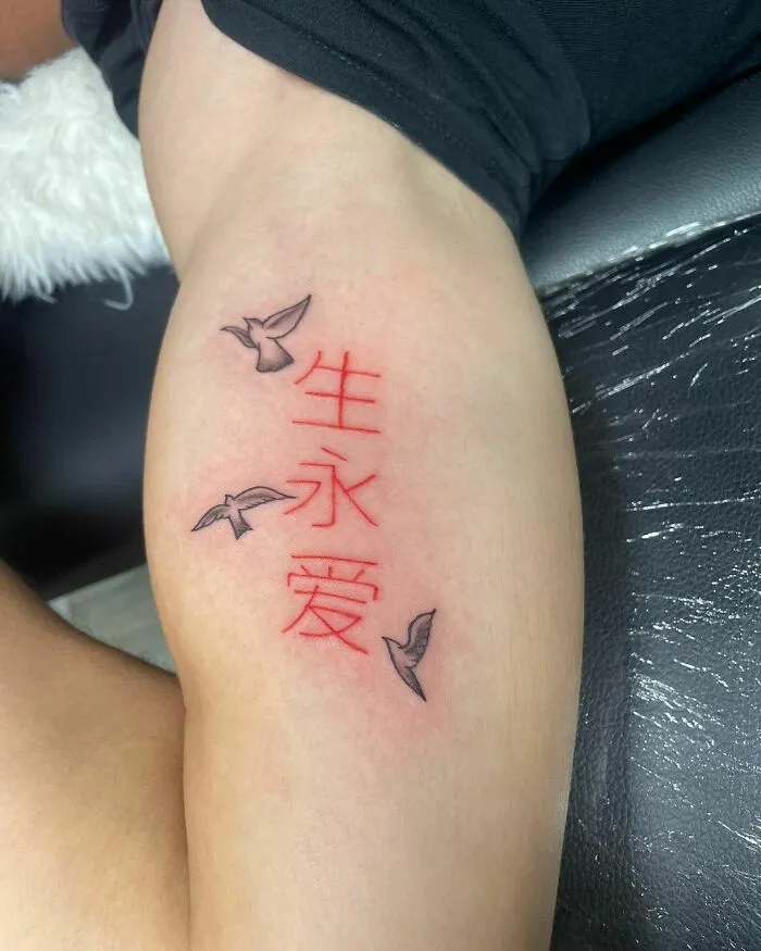 Red ink tattoo with Chinese characters and birds on an upper arm.