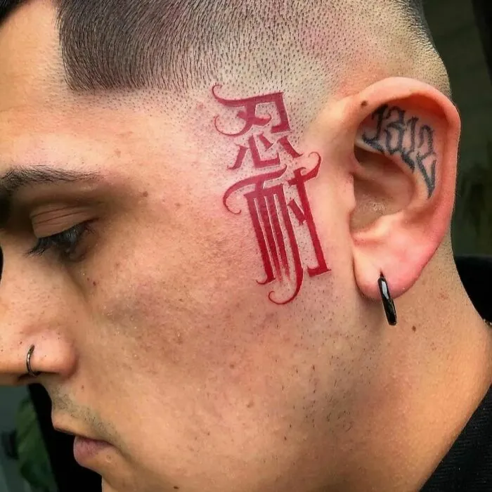 Side profile with a red ink tattoo of intricate lettering near the ear, showcasing bold tattoo art.
