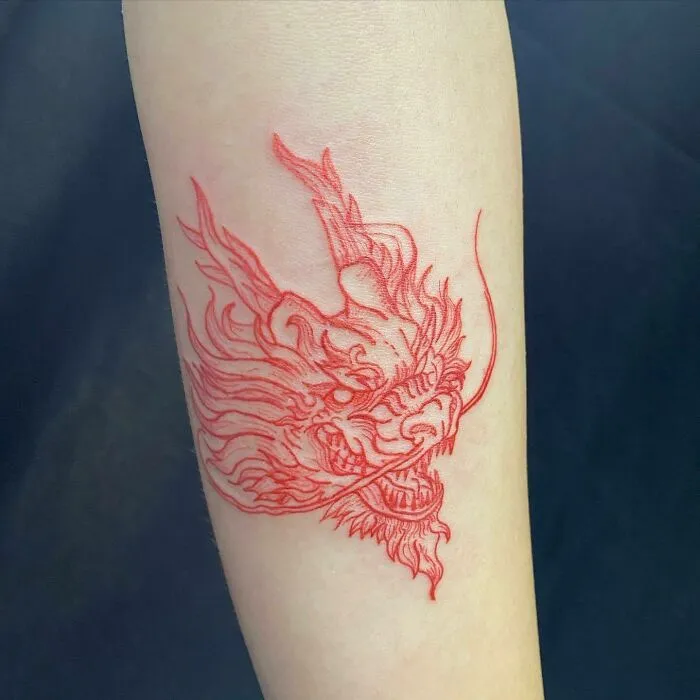 Red ink dragon tattoo design on forearm, showcasing intricate details and bold lines.