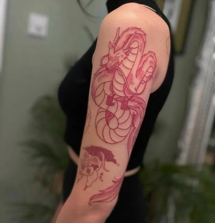 A red ink tattoo of a serpent design on a person's upper arm, showcasing intricate details.