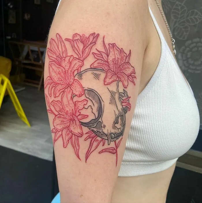 Red ink tattoo featuring a skull with floral designs on an upper arm.
