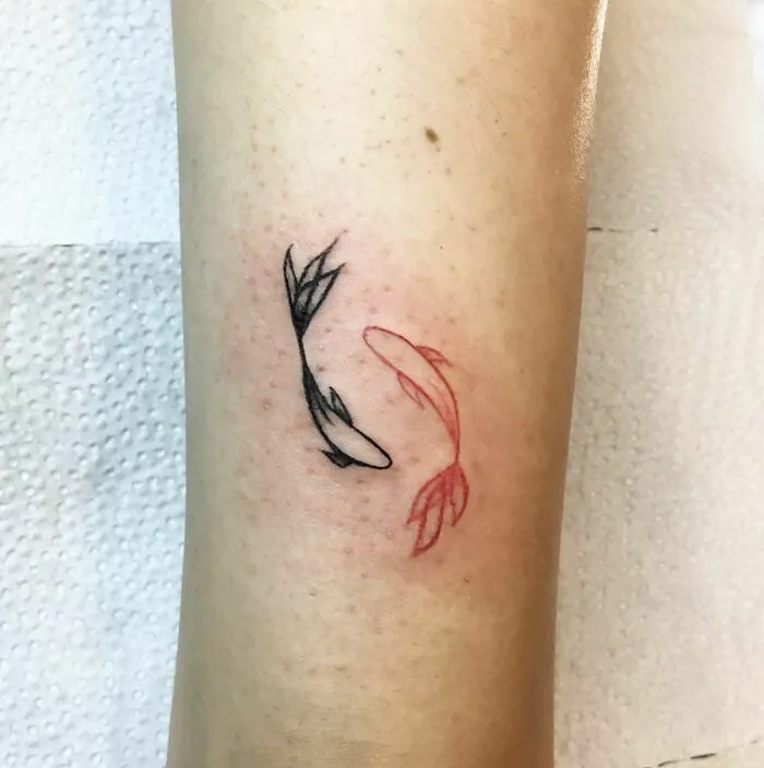 Red ink tattoo of koi fish on forearm, blending red and black designs.