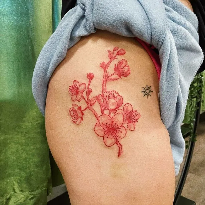 Red ink tattoo of blooming cherry blossoms on a thigh, showcasing detailed floral design.