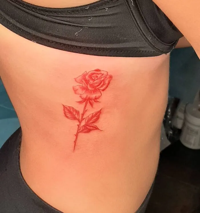 Red ink tattoo of a rose on skin, showcasing intricate details and vibrant color.