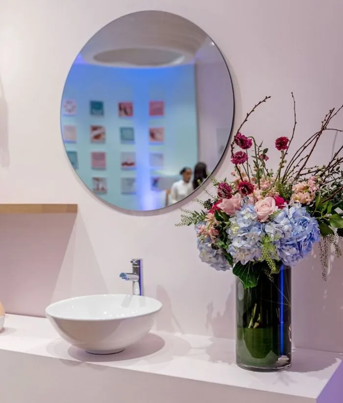 Modern home decoration with round mirror, white sink, and a vase of colorful flowers.