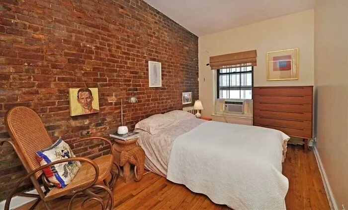 Cozy bedroom with exposed brick wall, wicker chair, and warm decor.