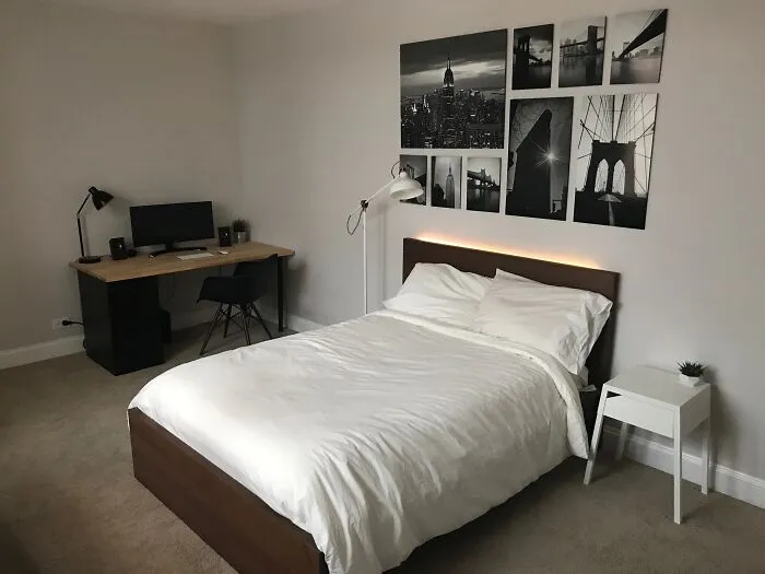 Modern bedroom with minimal decoration, white bed, desk setup, and black-and-white cityscape photos on the wall.