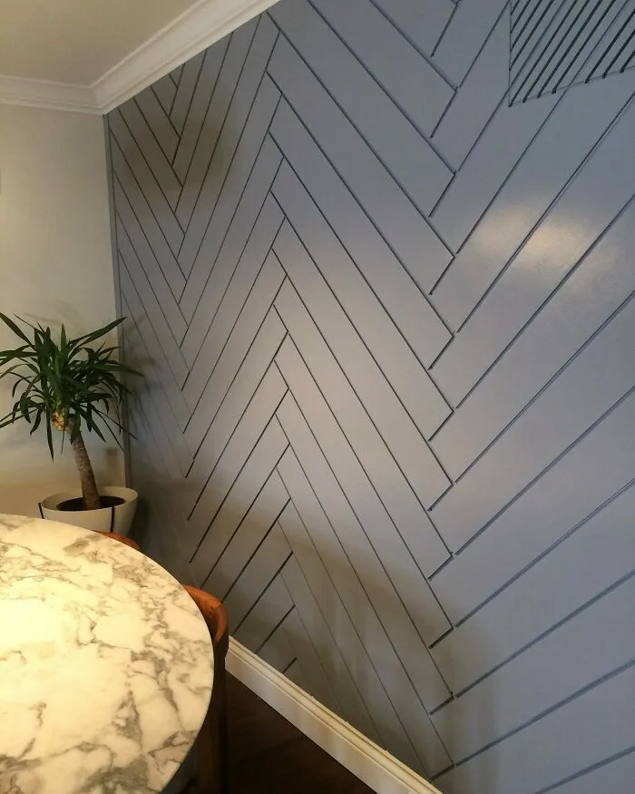 Chevron-patterned accent wall in gray with a marble table and a potted plant, showcasing home decoration ideas.