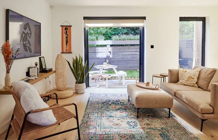 Cozy living room with modern home decoration, featuring a beige sofa, woven chair, and colorful rug near a garden view.