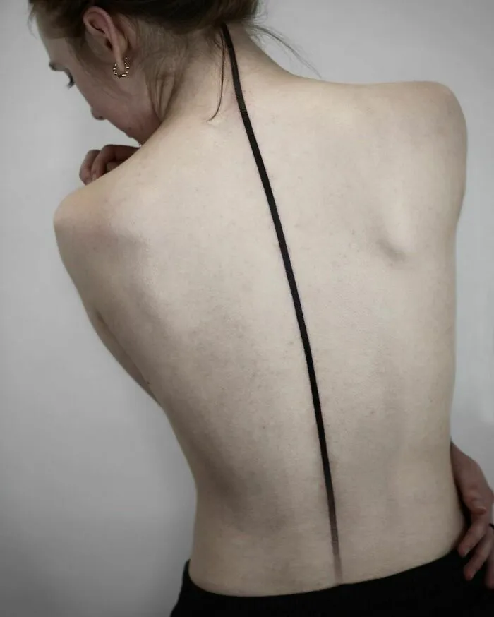 Elegant spine tattoo with a minimalistic black line design on a woman's back.