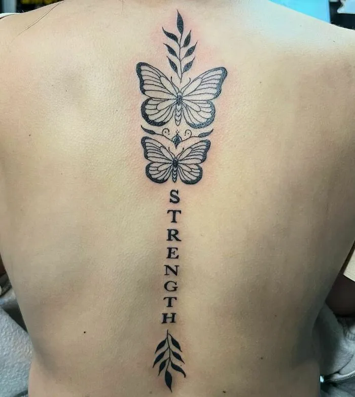 Butterfly spine tattoo with the word "strength" and decorative leaves, showcasing elegant tattoo ideas.