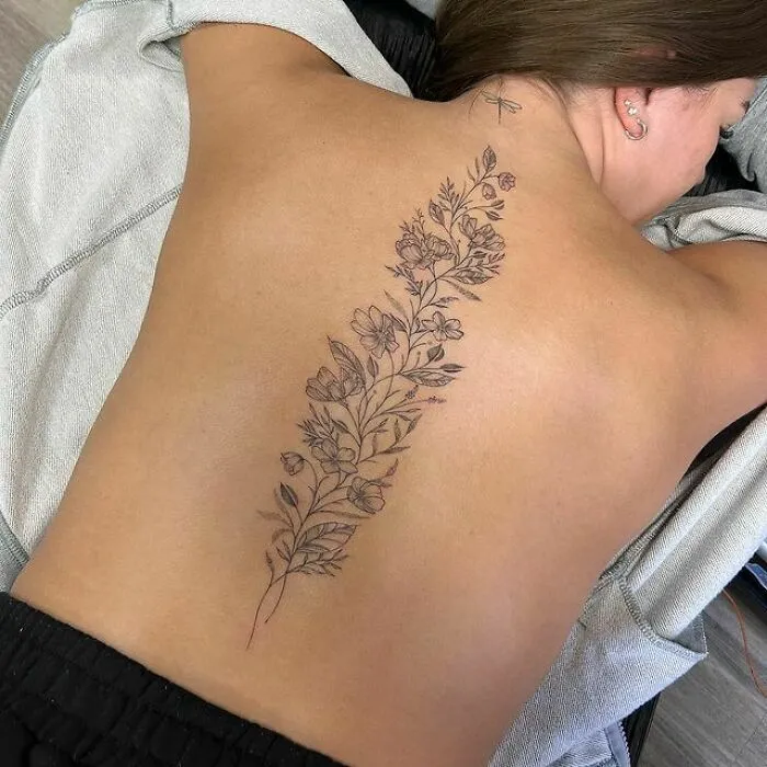 Floral spine tattoo on a woman's back, showcasing intricate linework and delicate flower details.