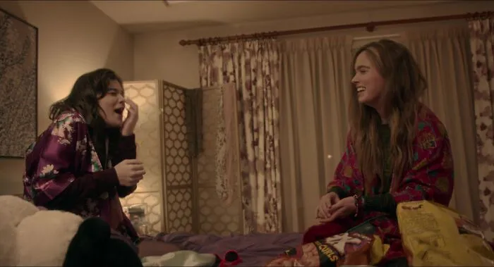 Two best friends laughing on a bed surrounded by snacks, creating a warm, friendly atmosphere.