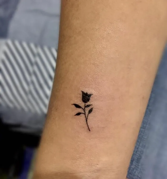 Small rose wrist tattoo design on forearm, showcasing minimalist floral art.
