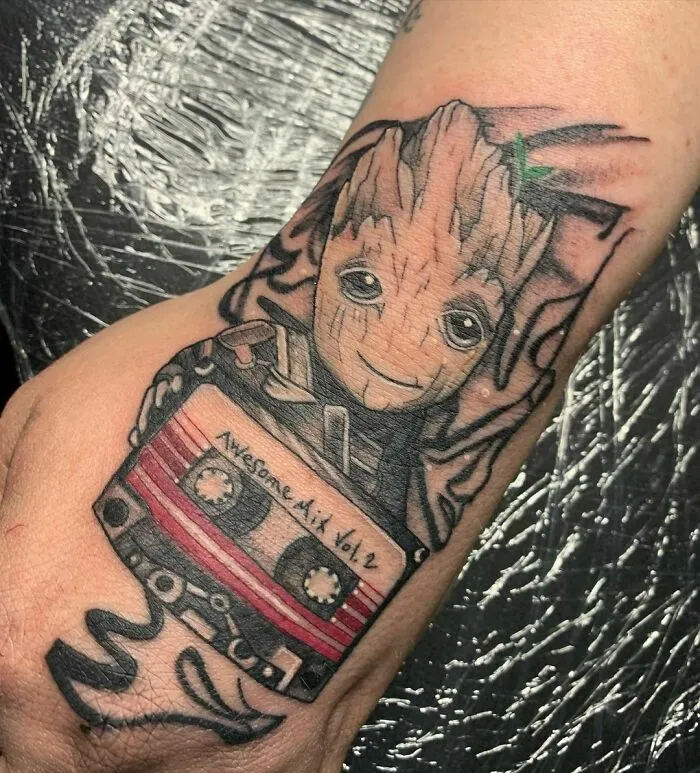 Marvel tattoo featuring Groot holding a cassette labeled "Awesome Mix Vol. 2" on a person's hand.