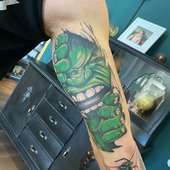 Marvel tattoo depicting Hulk's face tearing through skin on a person's arm, with vibrant green colors and detailed expression.