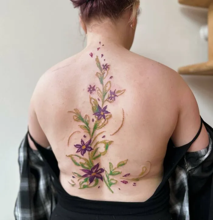 Elegant spine tattoo with purple and green floral design on a woman's back.