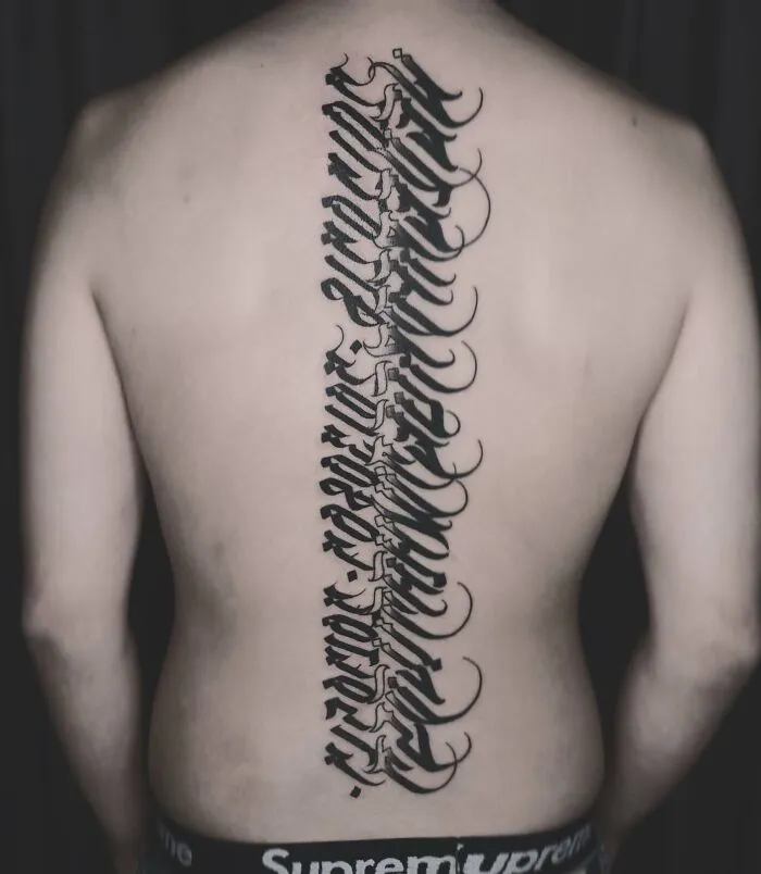 Elegant spine tattoo in bold script down the back, showcasing intricate design.