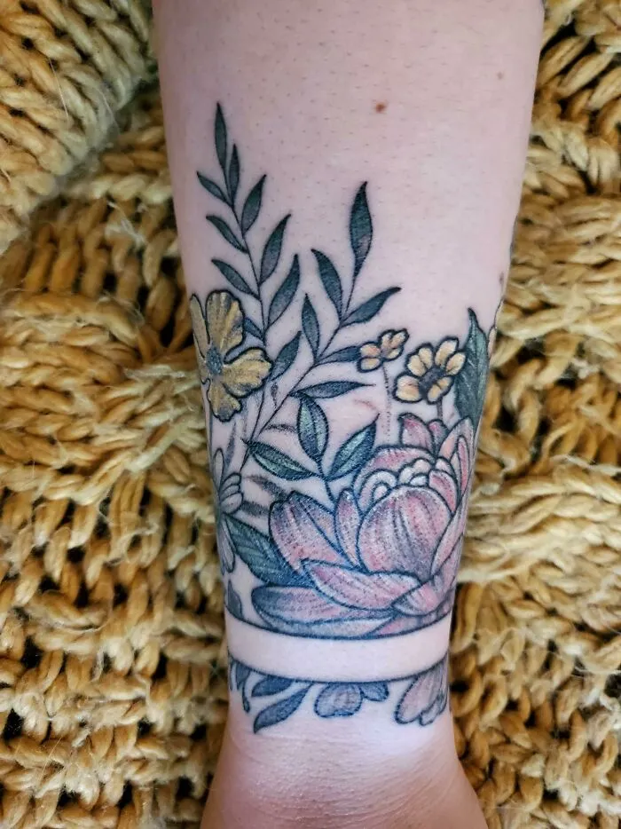 Floral wrist tattoo design featuring colorful flowers and leaves on a textured background.