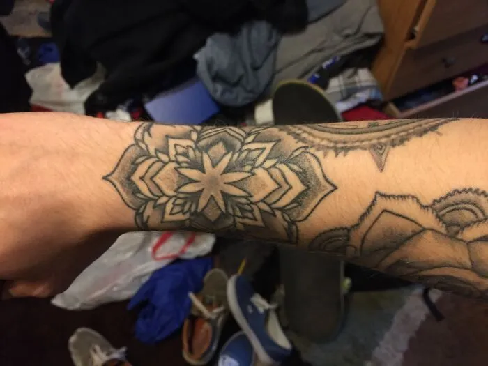 Geometric wrist tattoo design with floral patterns on forearm.