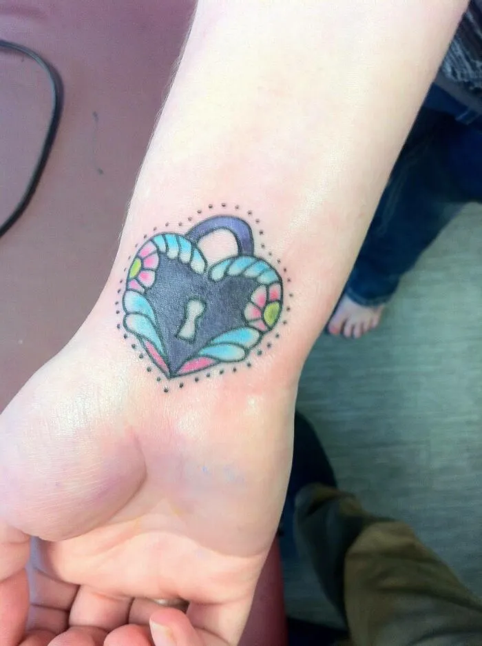 Colorful heart lock wrist tattoo with floral details.