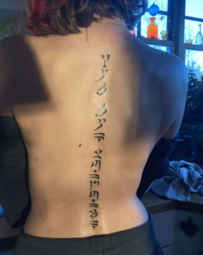 Elegant spine tattoo with intricate vertical script design.