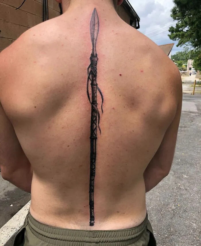Elegant spine tattoo resembling a detailed spear design on a person's back, showcasing intricate ink work.