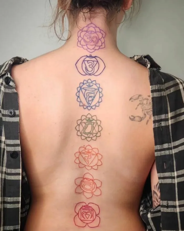 Elegant spine tattoo featuring colorful chakra symbols on a person's back.