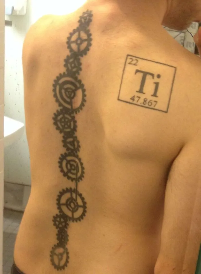 Elegant spine tattoo with mechanical gears design and titanium symbol on back.