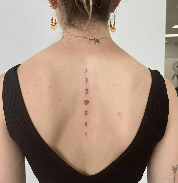 Elegant spine tattoo featuring moon phases on a woman's back, accented by a black dress.