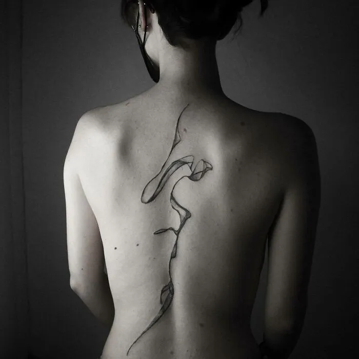 Intricate elegant spine tattoo design on a woman's back, showcasing fine abstract lines.