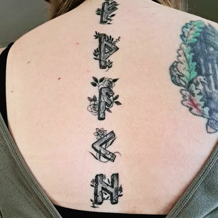Floral spine tattoo with geometric elements on a woman's back.