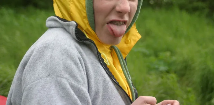 A child making a funny face outdoors, wearing a yellow hood, related to hurtful comments by parents.