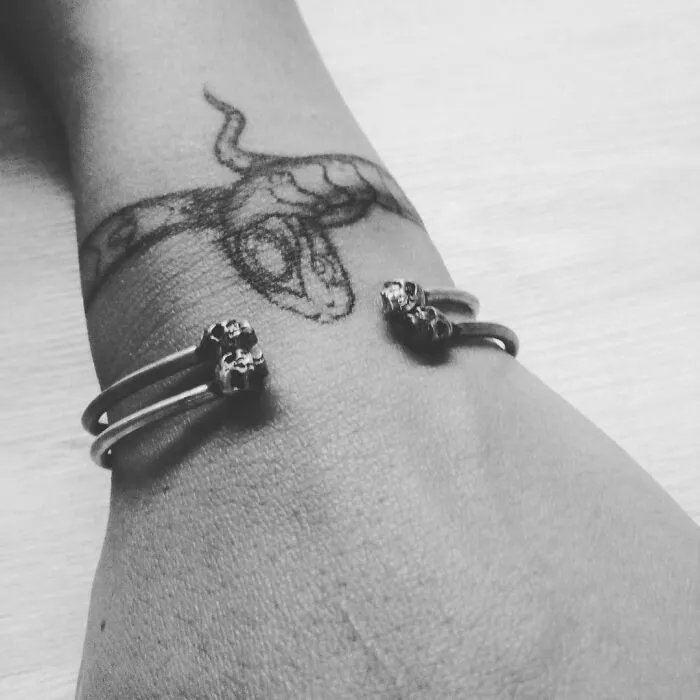 Wrist tattoo design featuring a snake wrapped around the arm, accompanied by a metal bracelet.