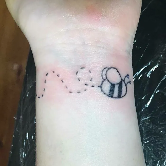 Wrist tattoo featuring a small bee with a dotted flight path.