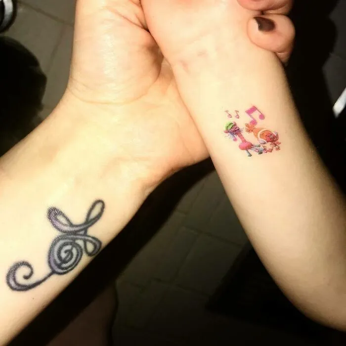 Two wrist tattoos: an elegant treble clef design and a colorful unicorn with musical notes.