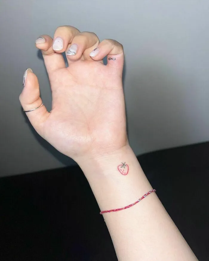 Small heart wrist tattoo design featuring a minimalist strawberry on a person’s arm.