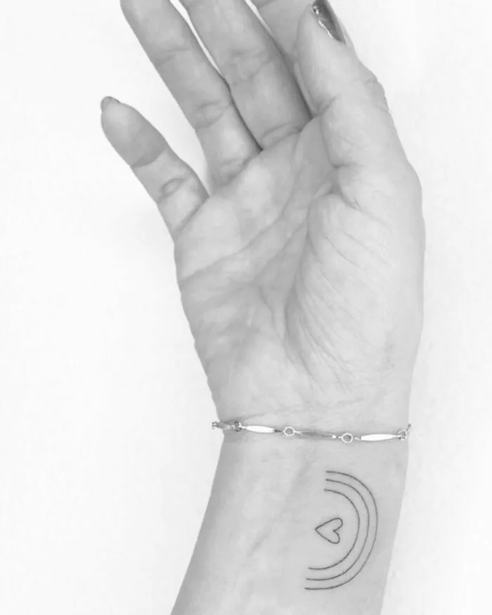 Minimalist wrist tattoo featuring concentric lines and a small heart design.